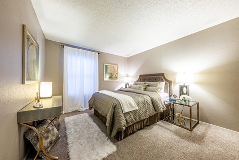 Model bedroom with large bed and dresser at Hillside Creek Apartments in Austin, TX